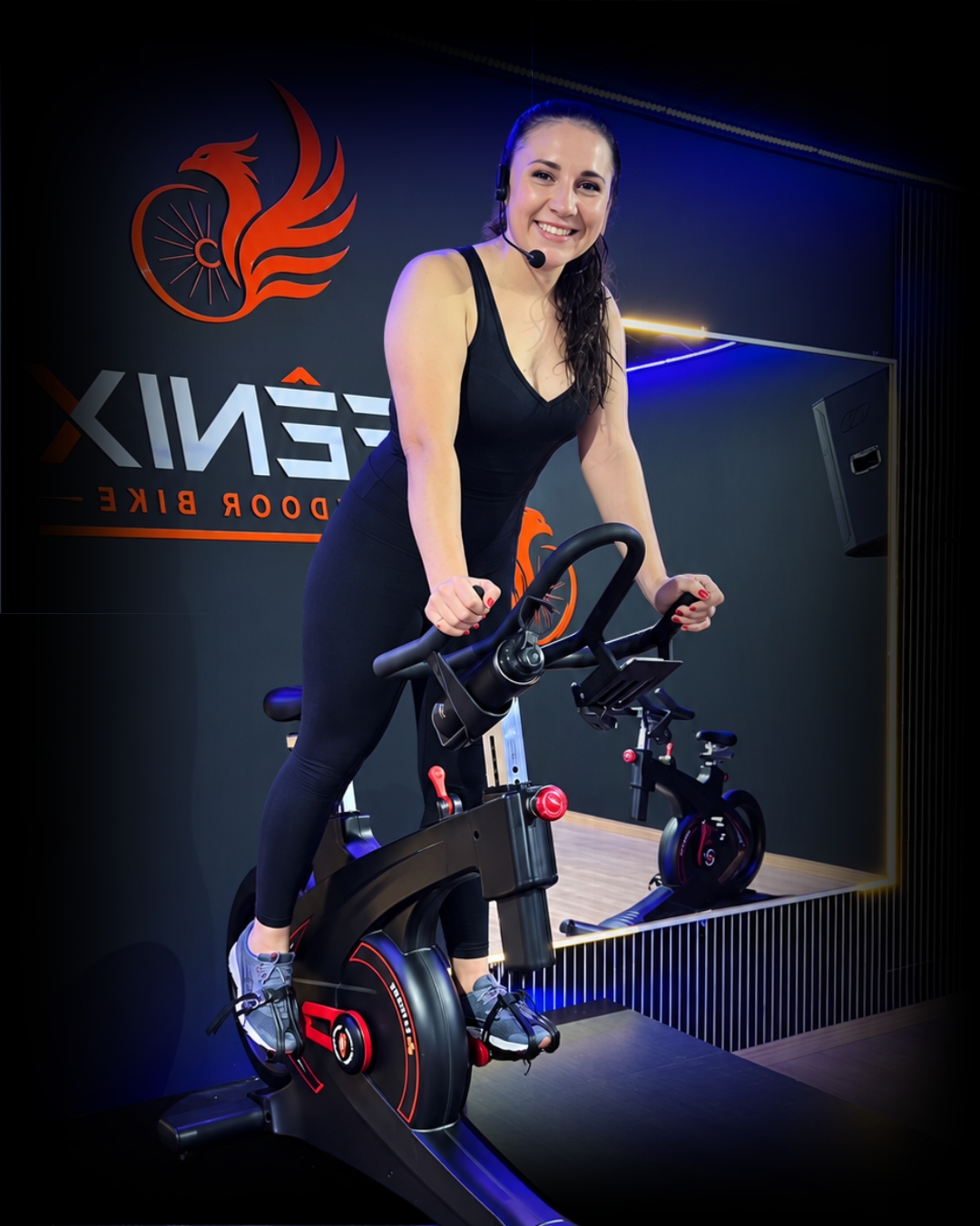 Professora de preto na bicicleta, no estúdio Fênix Indoor Bike com iluminação azul